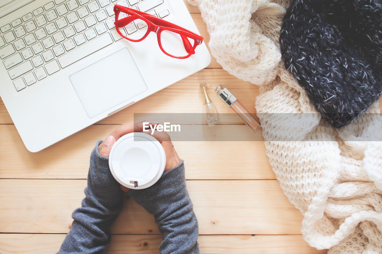 Directly above shot of cropped hands holding coffee cup at table