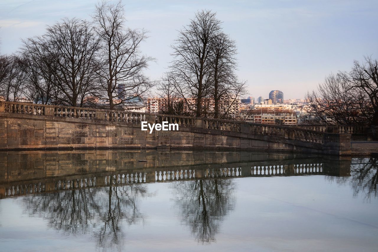 REFLECTION OF BARE TREES ON RIVER AGAINST SKY