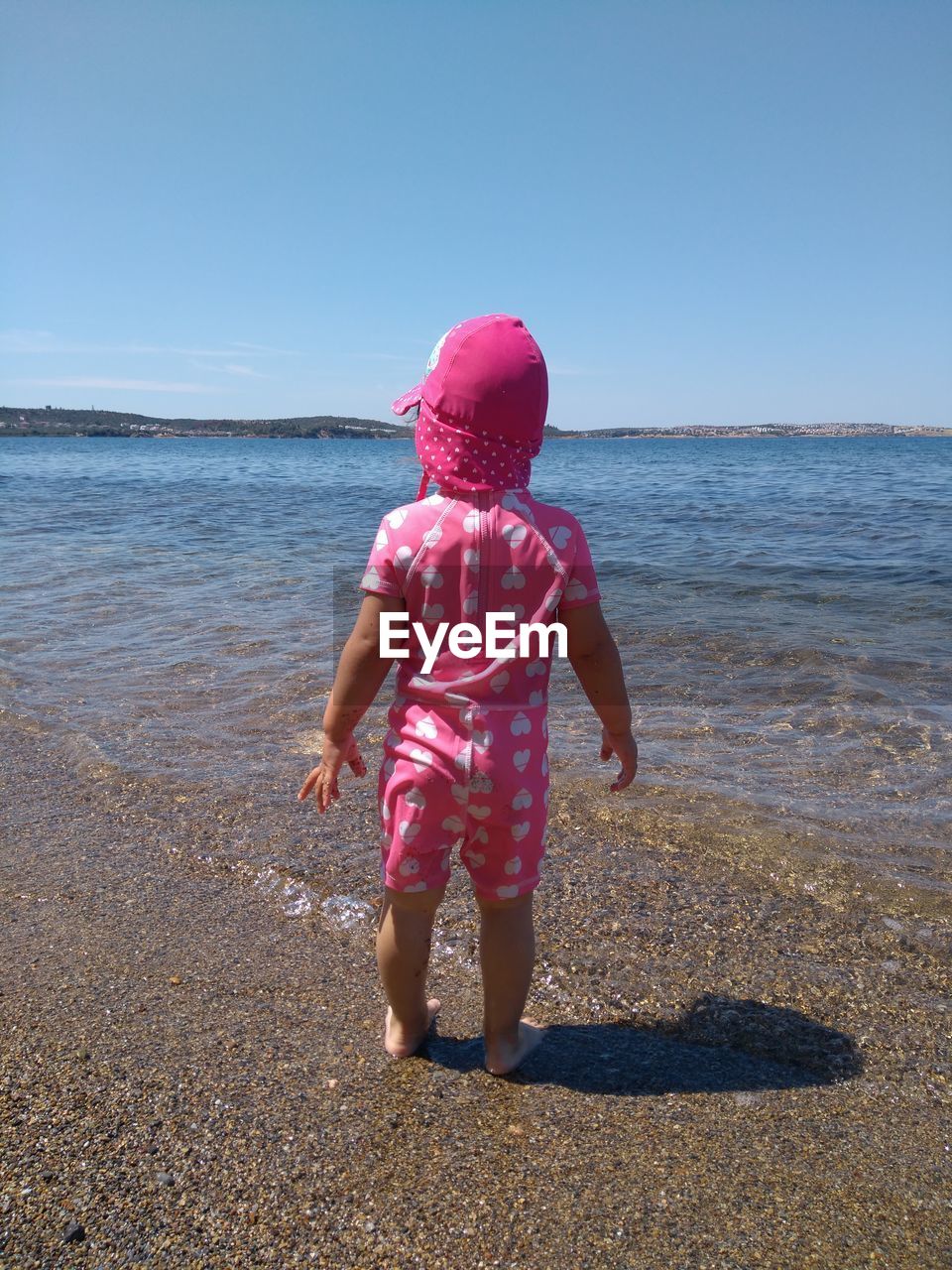Rear view of baby girl standing at beach against sky