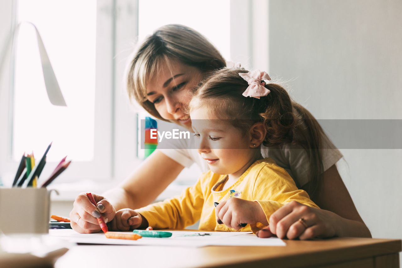 A young mother teaches her little daughter to draw with colored pencils. time together, creativity