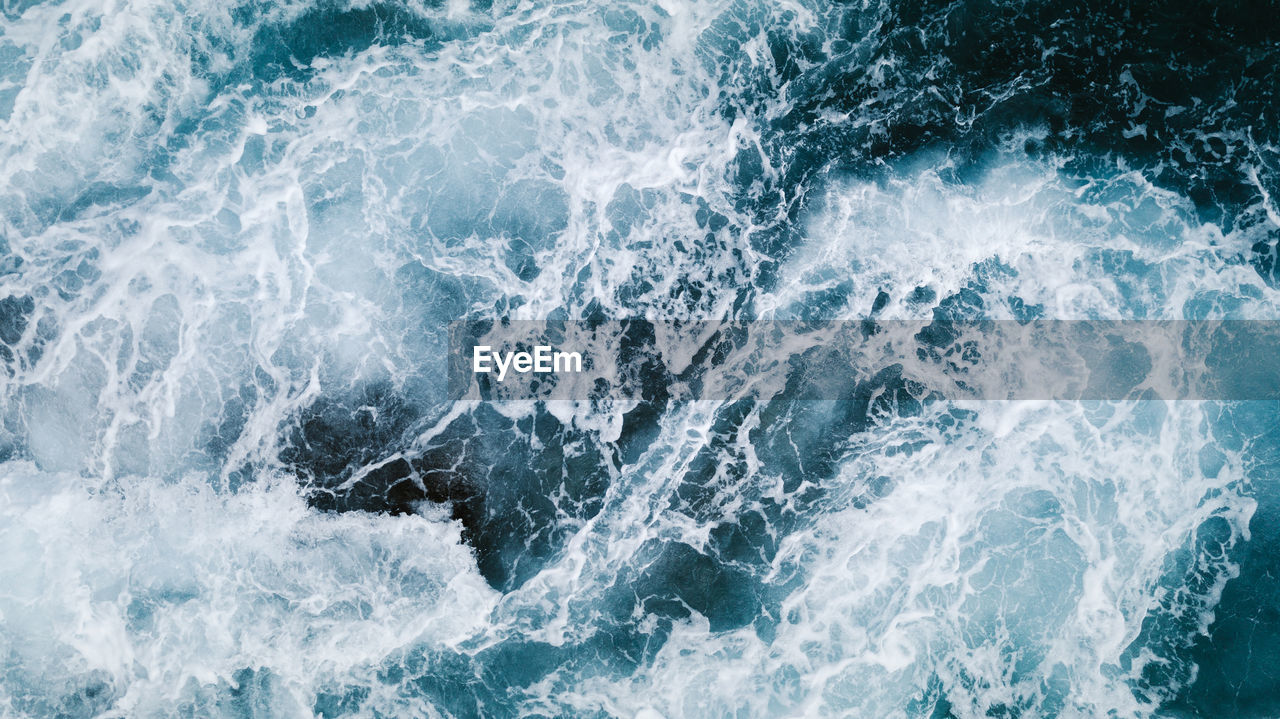 From above aerial view of turquoise ocean water with splashes and foam for abstract natural background and texture