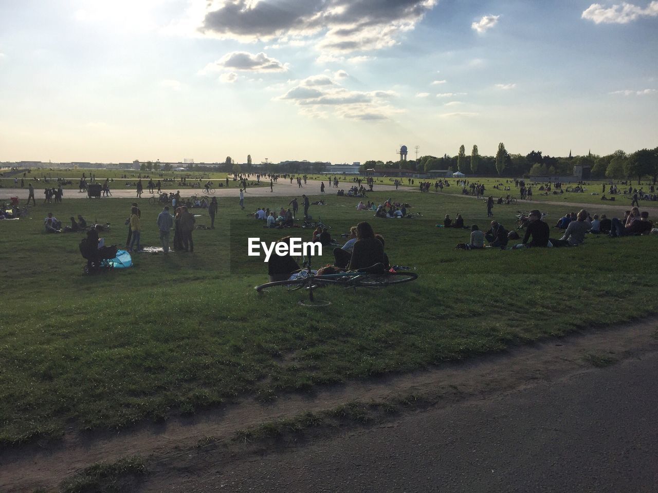 PEOPLE ON GRASSY FIELD AGAINST CLOUDY SKY