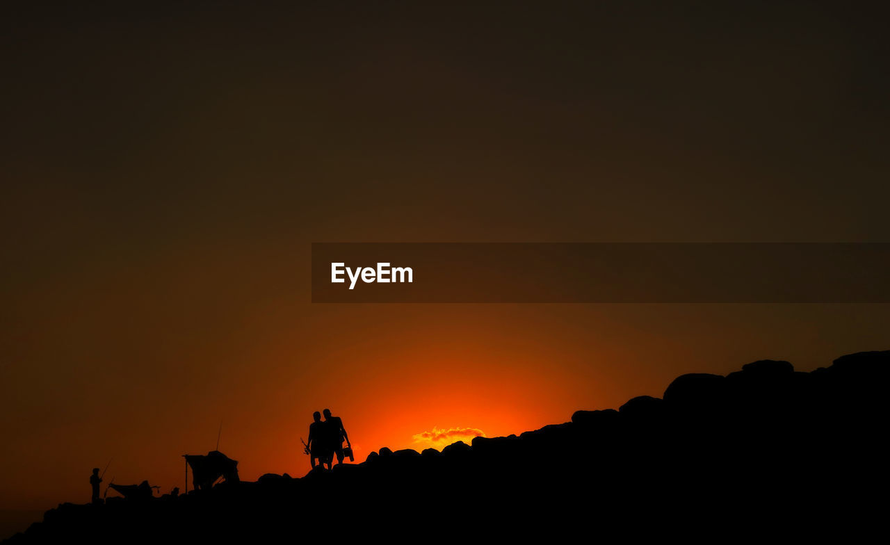 Silhouette people on field against orange sky during sunset