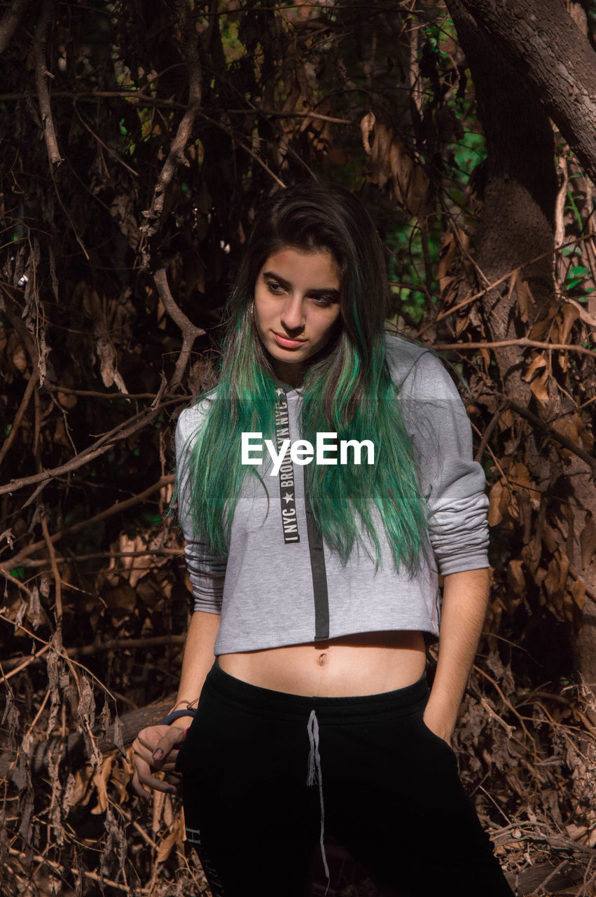 Thoughtful young woman looking away against trees in forest