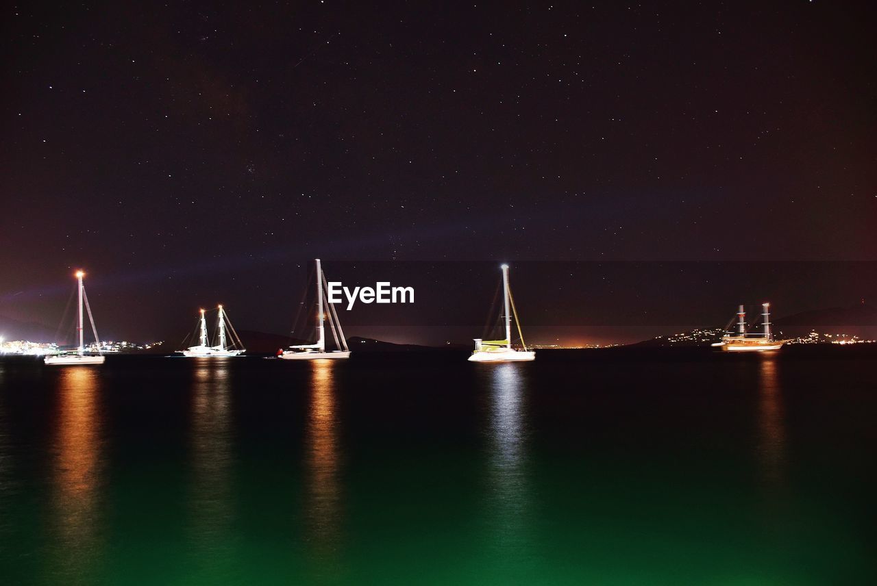 SAILBOATS MOORED IN SEA AGAINST SKY AT NIGHT