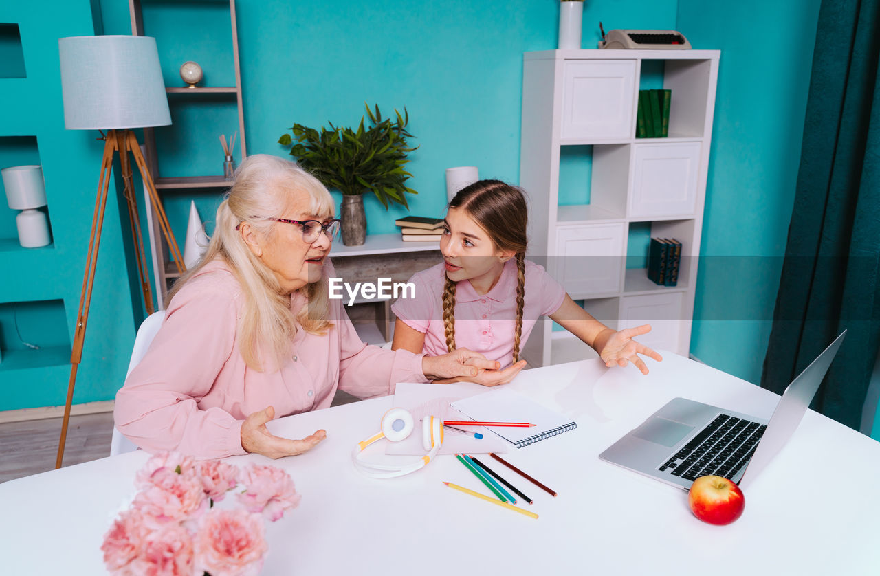 Surprised grandmother and granddaughter gesturing while looking at laptop