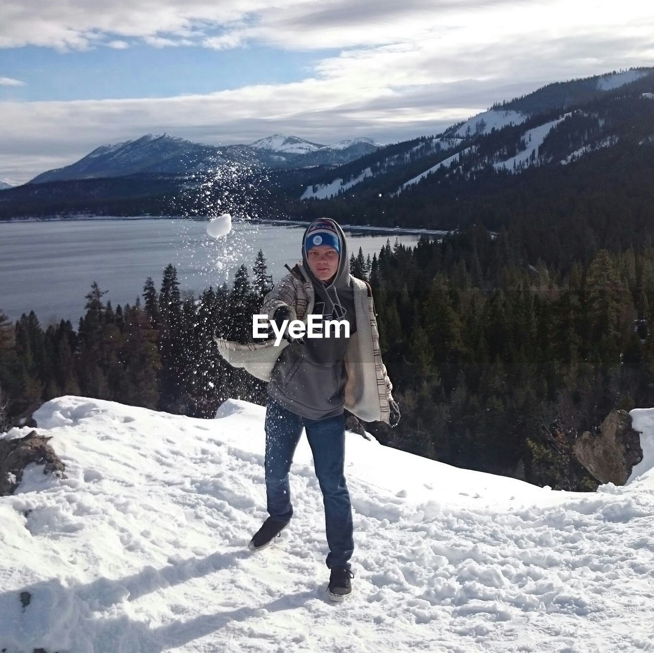 Portrait of man throwing snowball during winter while standing against mountain range
