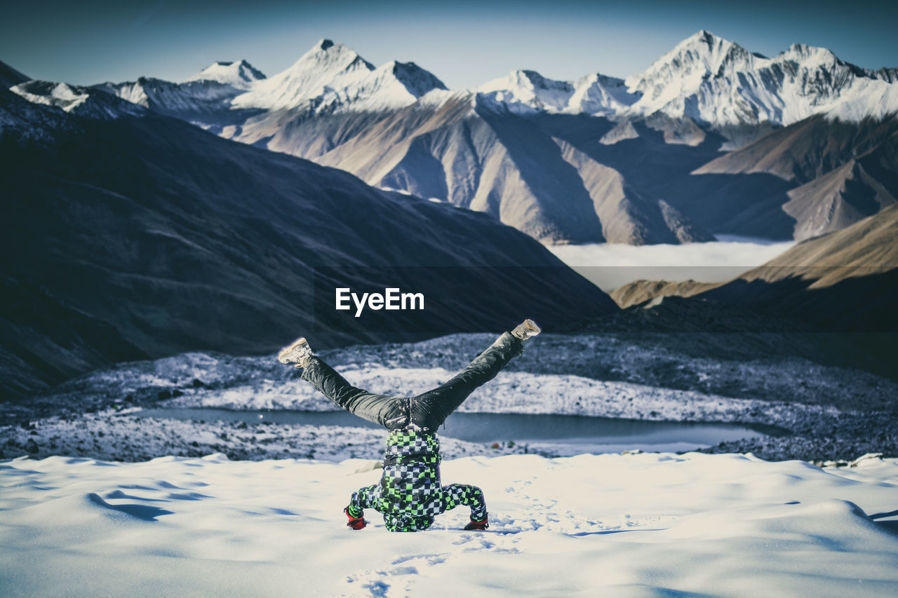 Young man doing headstand against mountains on snow