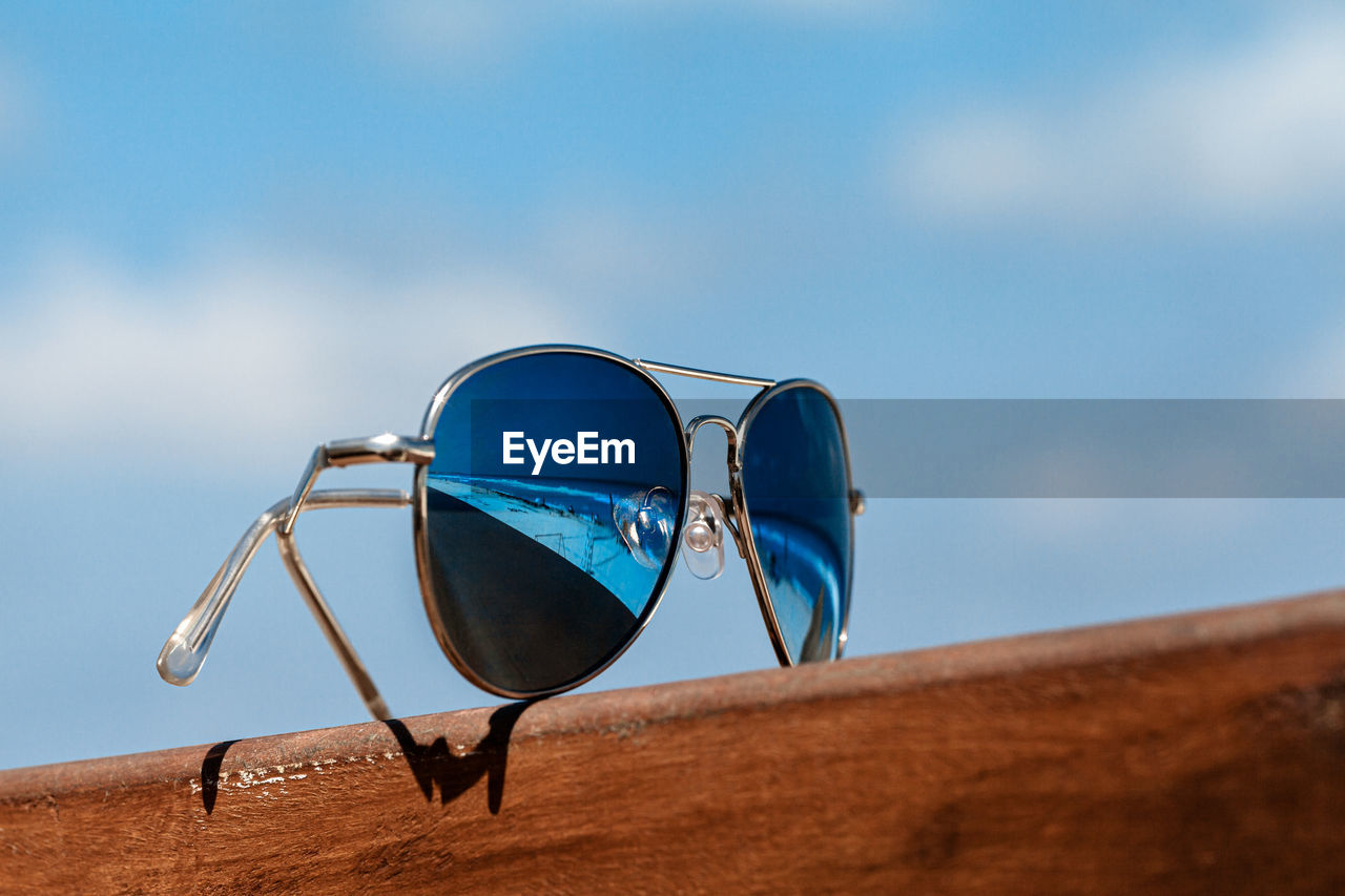 CLOSE-UP OF SUNGLASSES ON LAND AGAINST SKY