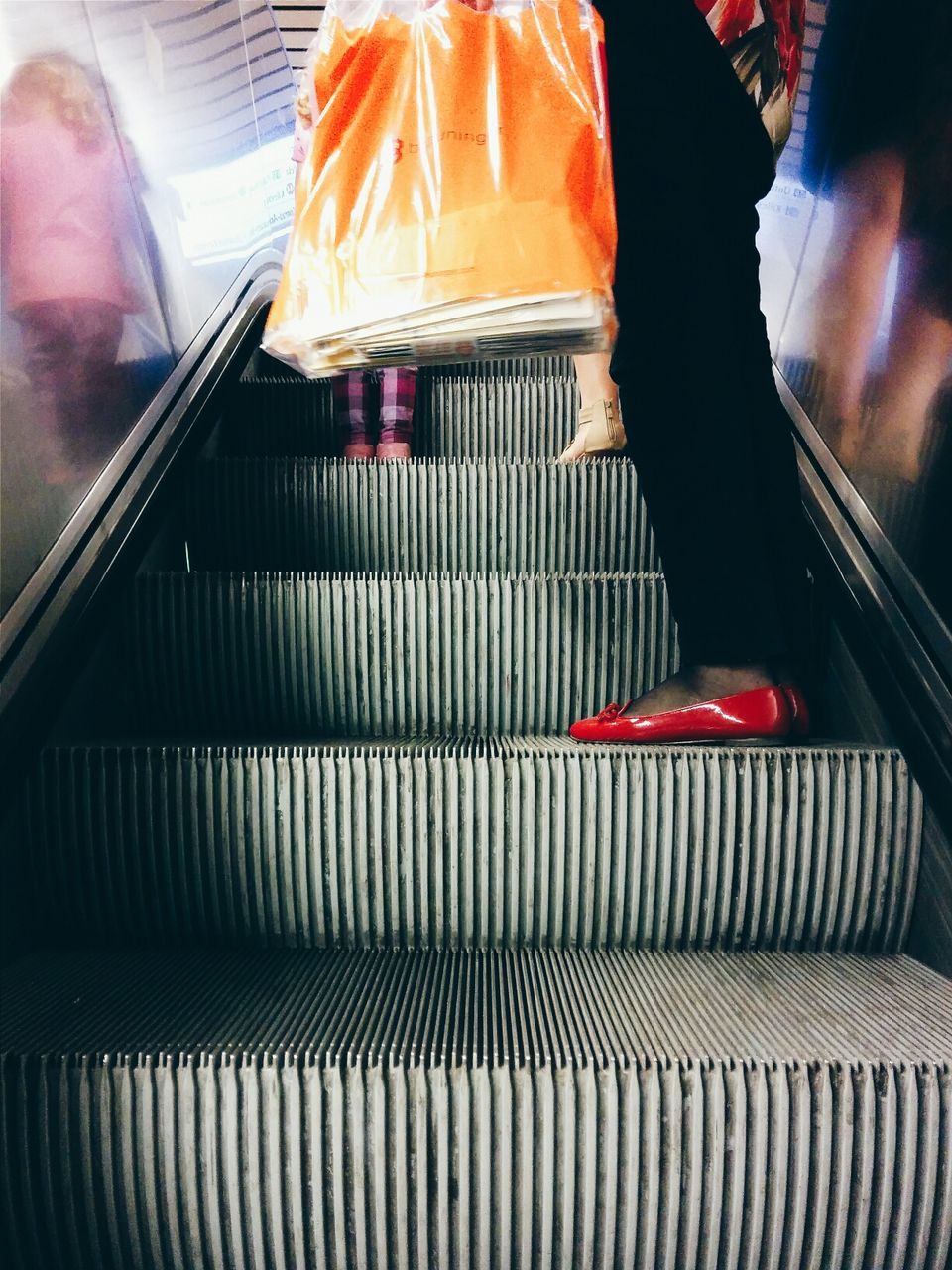 Low section of two people standing on escalator