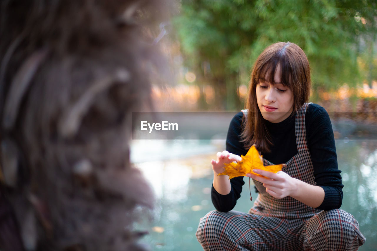 Woman holding maple leaf against lake