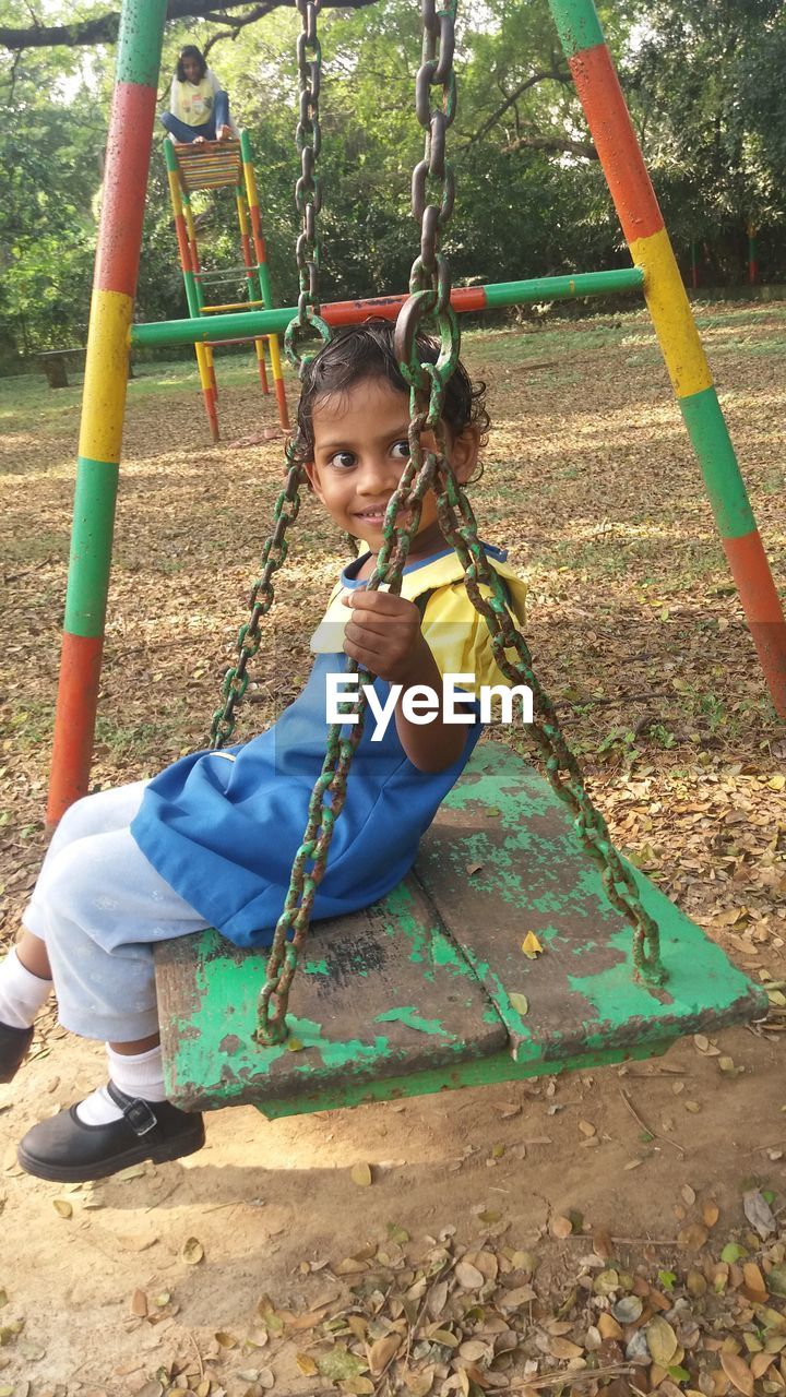 Portrait of smiling girl sitting on swing in playground