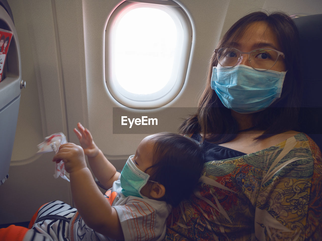 Mother and daughter wearing mask while sitting by window in airplane