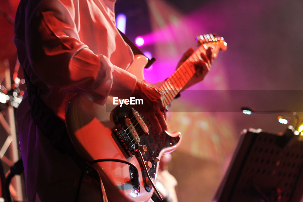 Midsection of man playing guitar in music concert