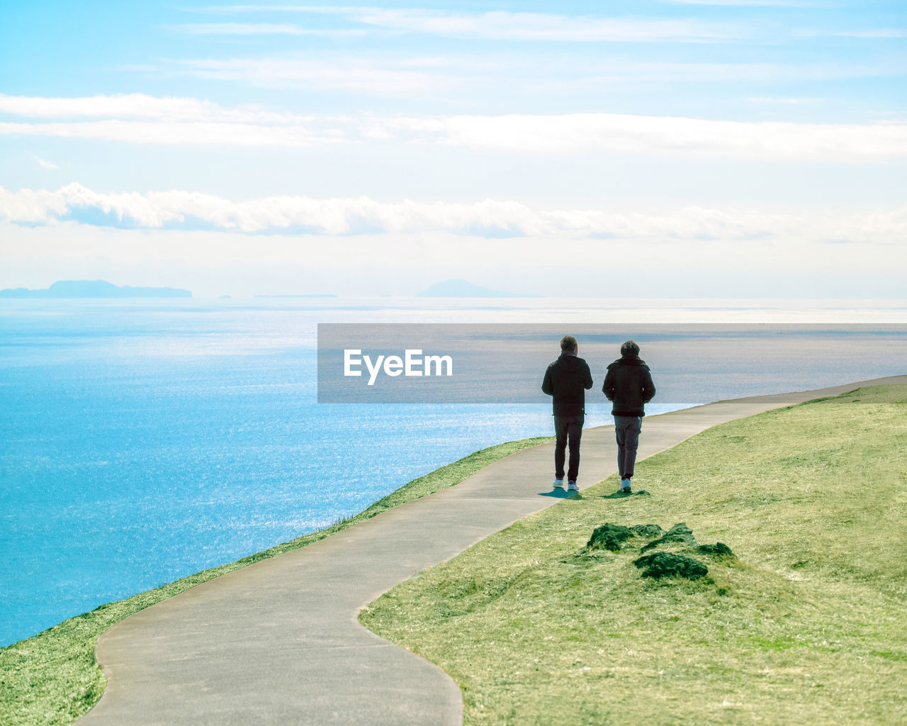 REAR VIEW OF MEN STANDING ON SHORE AGAINST SKY