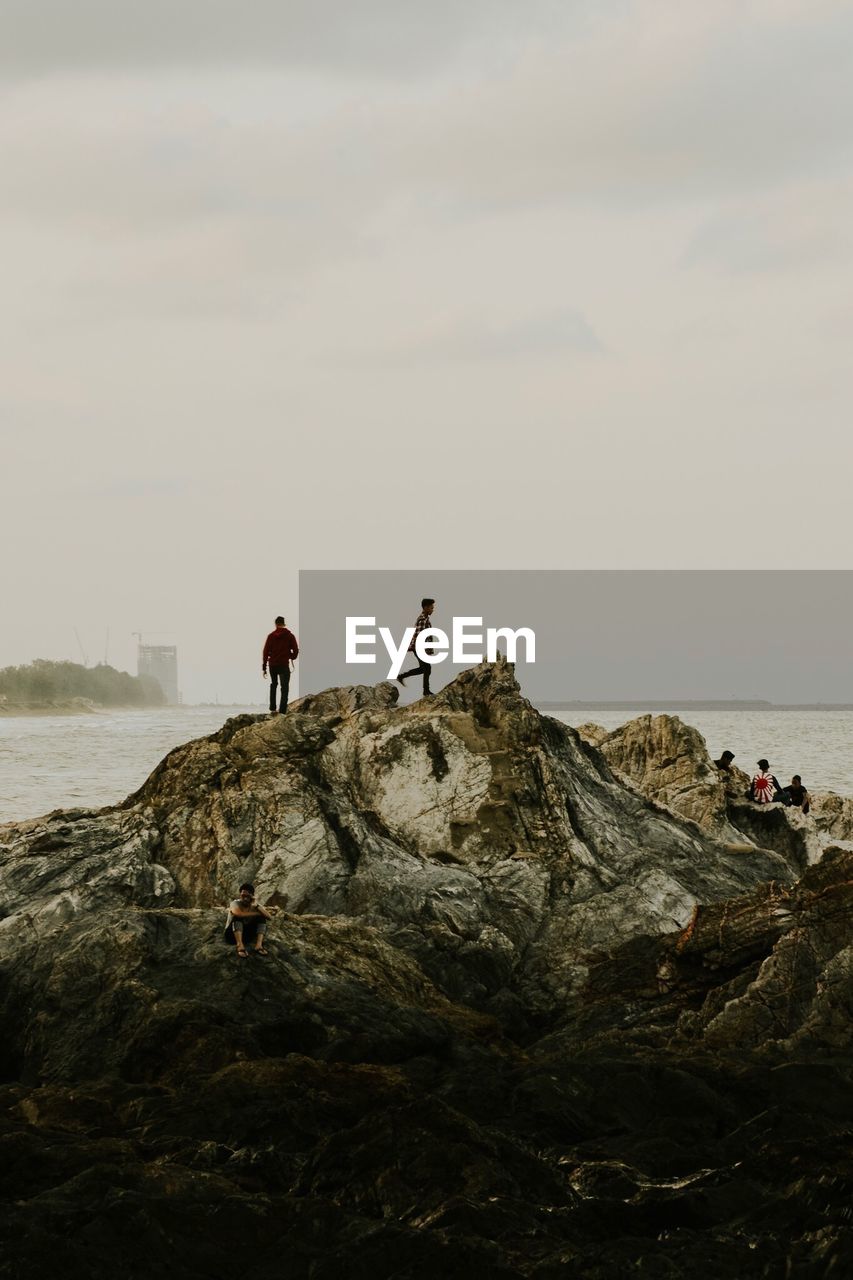 Men on rocky shore against sky
