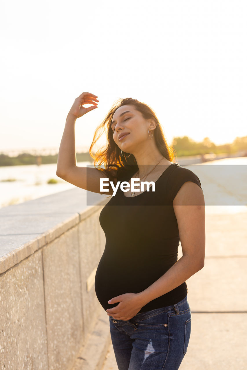 BEAUTIFUL YOUNG WOMAN STANDING AGAINST SKY