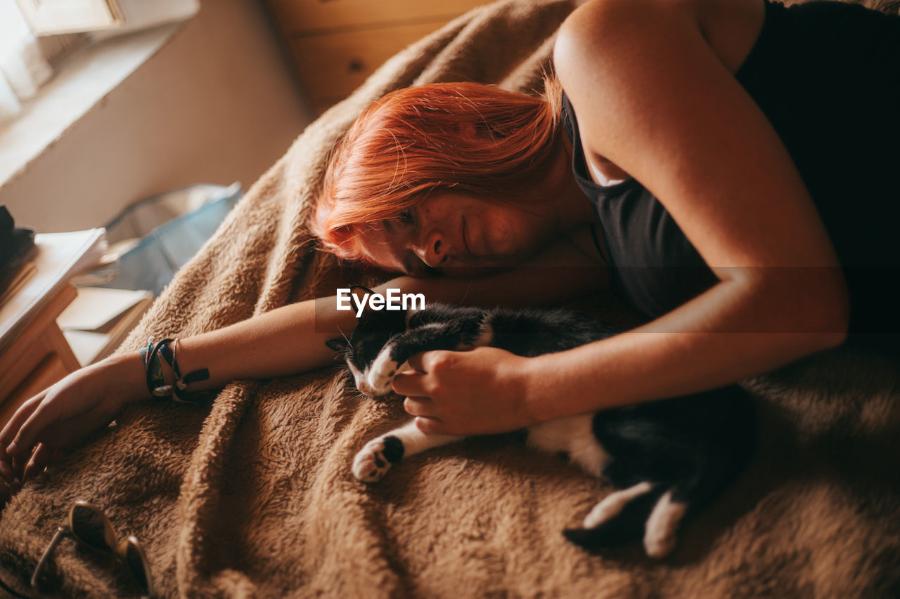 High angle view of woman lying on bed with cat at home