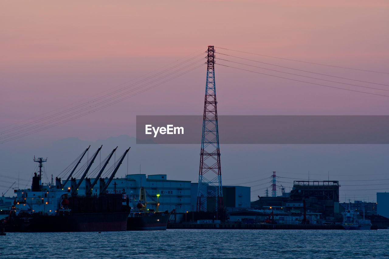 Cranes at commercial dock against sky during sunset