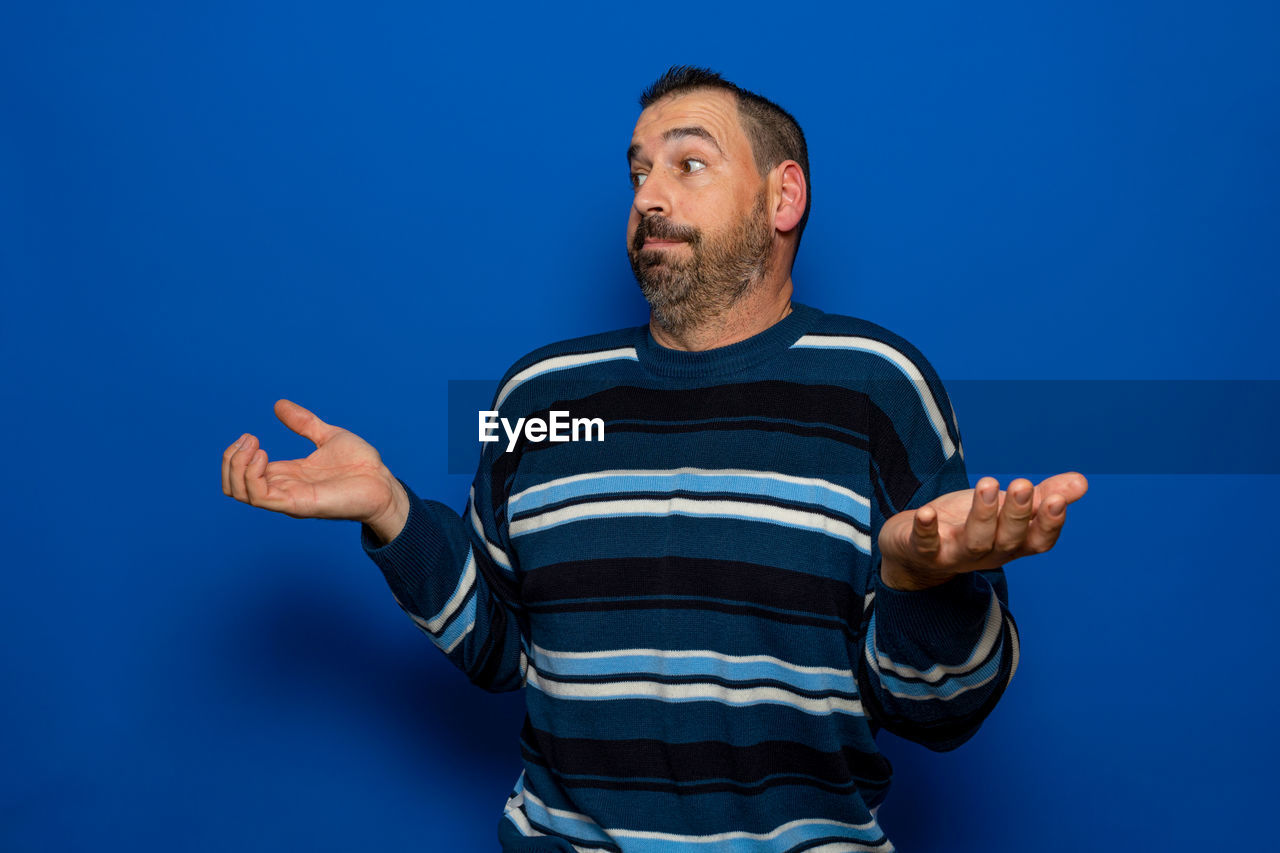 blue, one person, studio shot, colored background, adult, men, blue background, striped, casual clothing, indoors, waist up, facial hair, emotion, portrait, person, beard, young adult, gesturing, front view, looking, sports, happiness, standing, hand, copy space, lifestyles, sign language, smiling, clothing