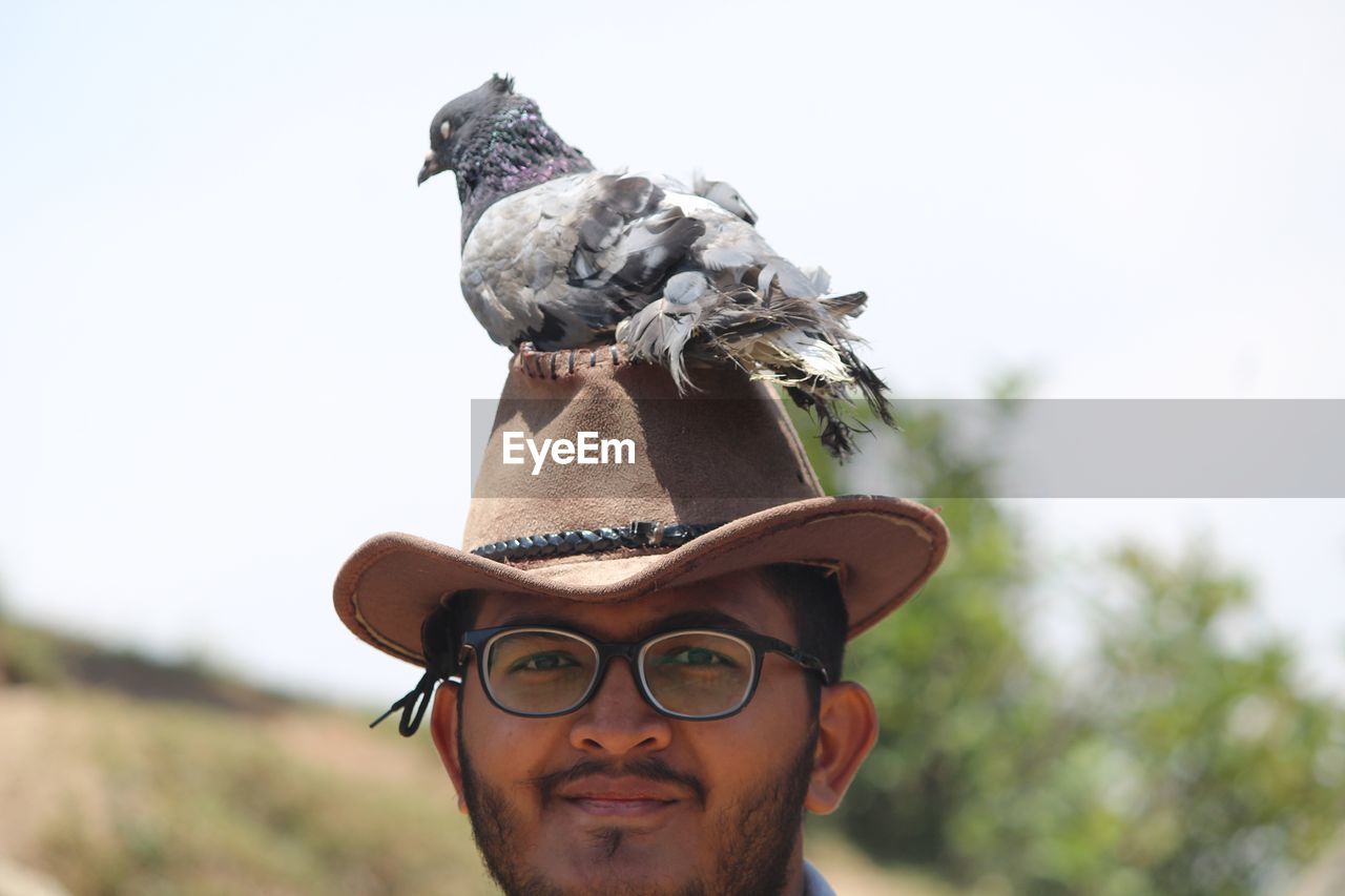 Close-up portrait of smiling young man wearing hat with pigeon on head