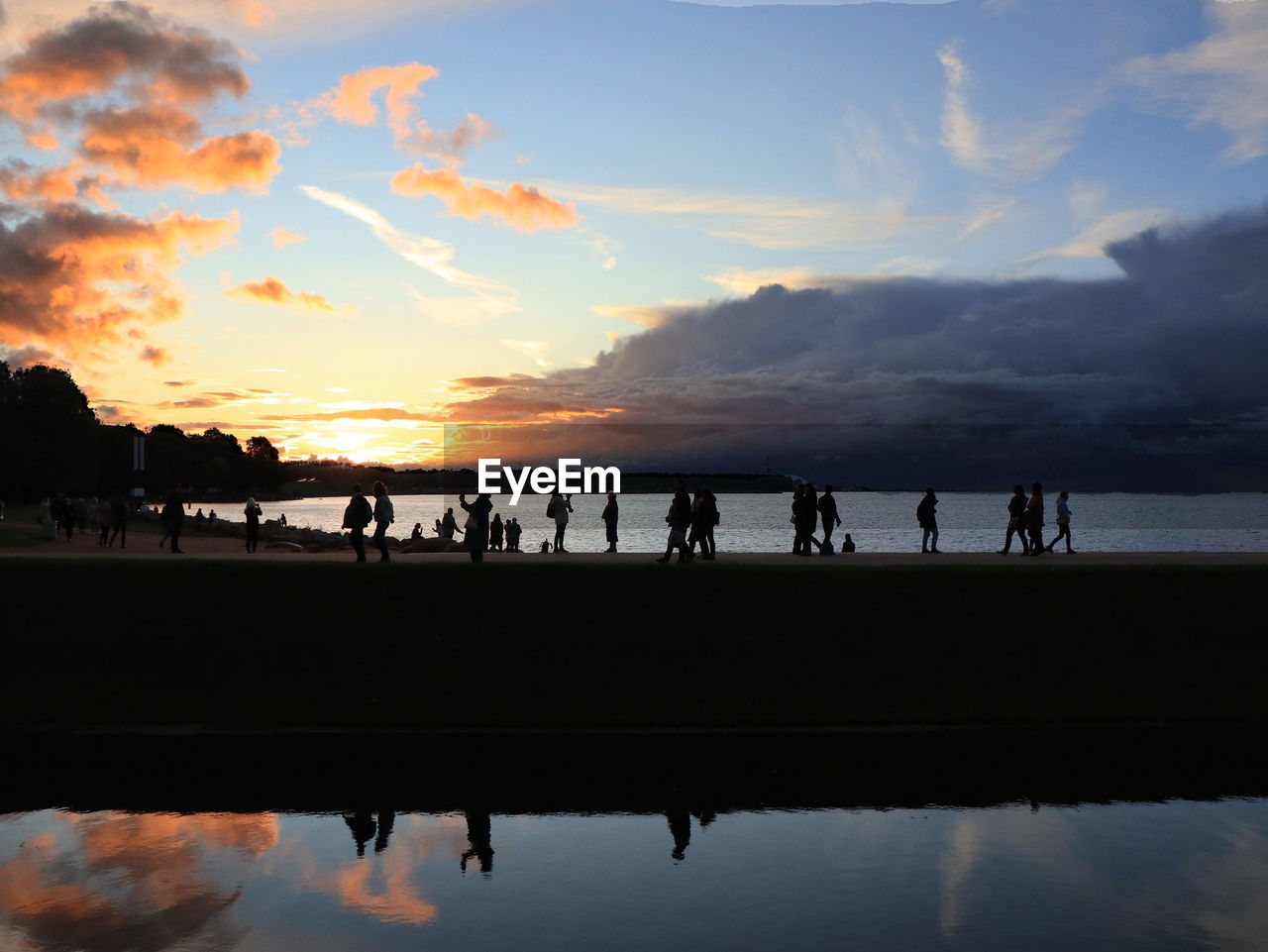 Silhouette people on bridge by lake against sky during sunset