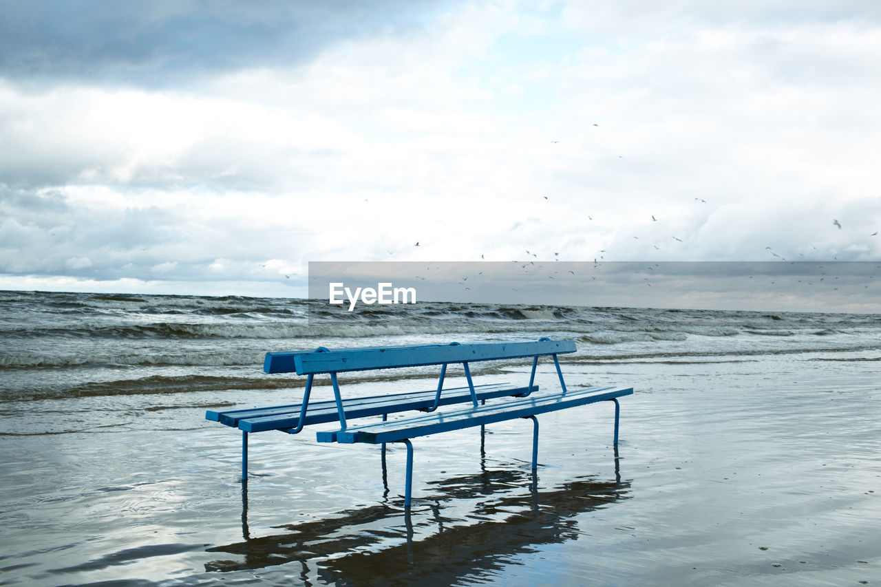 Empty bench at beach against sky