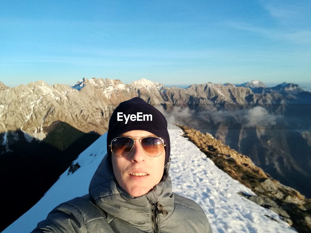 Portrait of young man wearing sunglasses standing against mountain range during winter