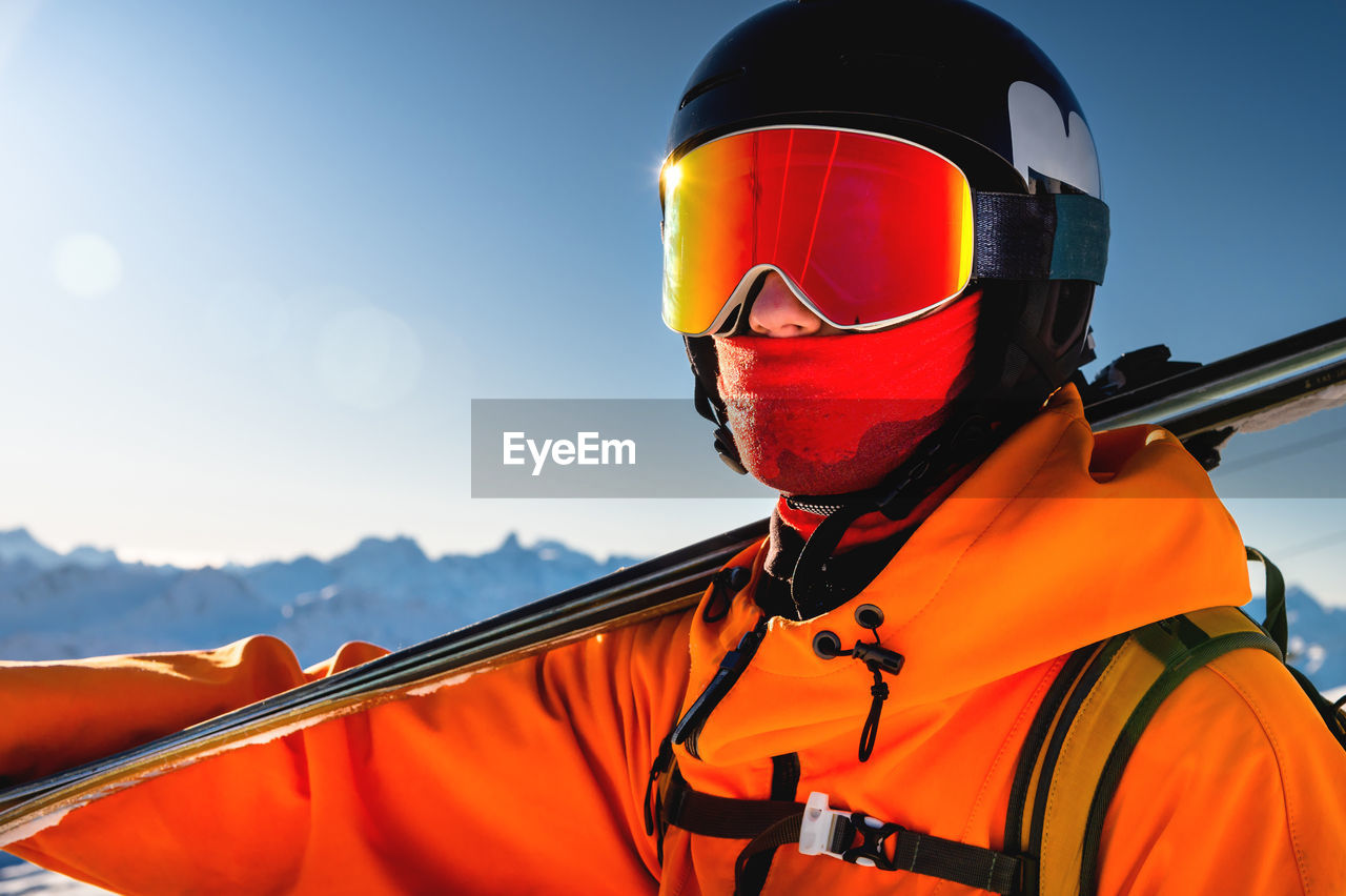 Portrait of a skier with skis on his shoulder. guy on a background of a mountain range on a sunny