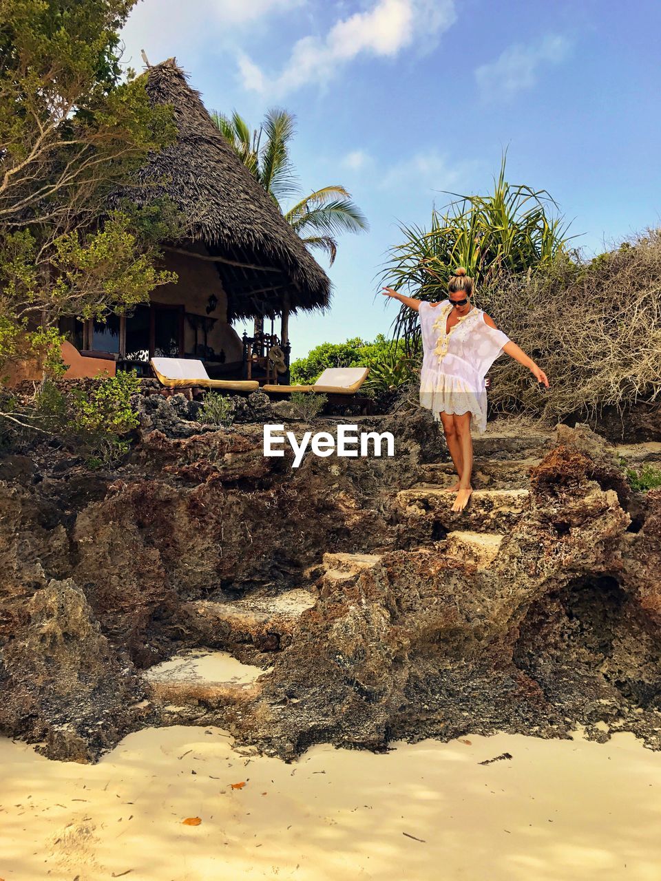 Woman standing on rock steps at beach against sky