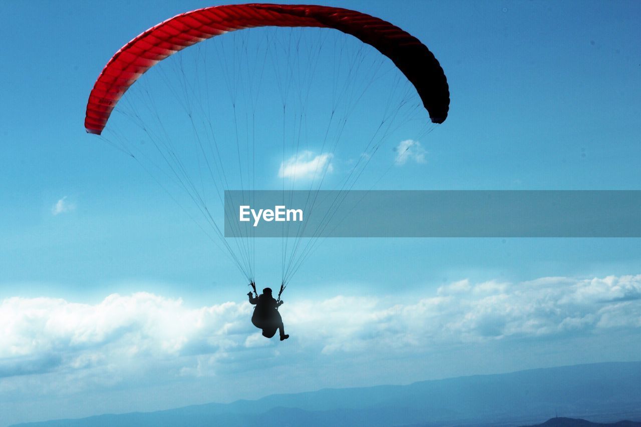 Low angle view of person paragliding against blue sky