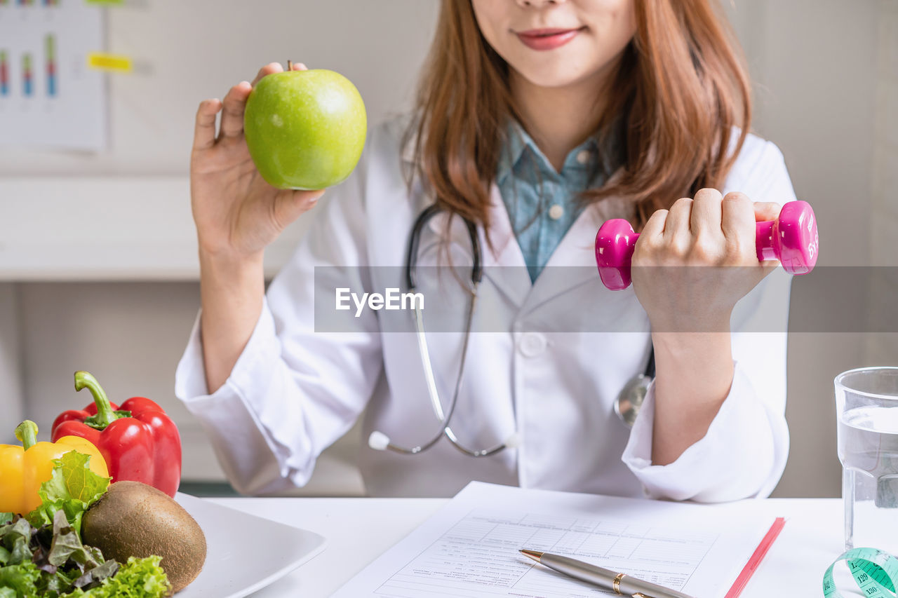 MIDSECTION OF WOMAN HOLDING APPLE AT HOME