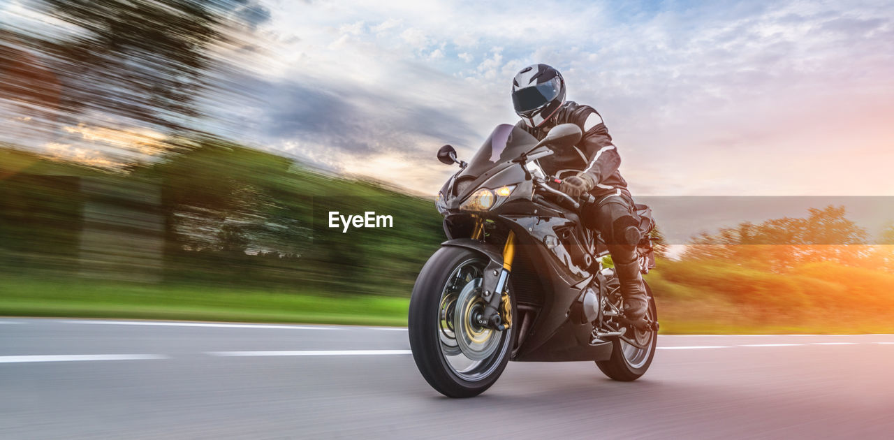 Man riding motorcycle on road against cloudy sky