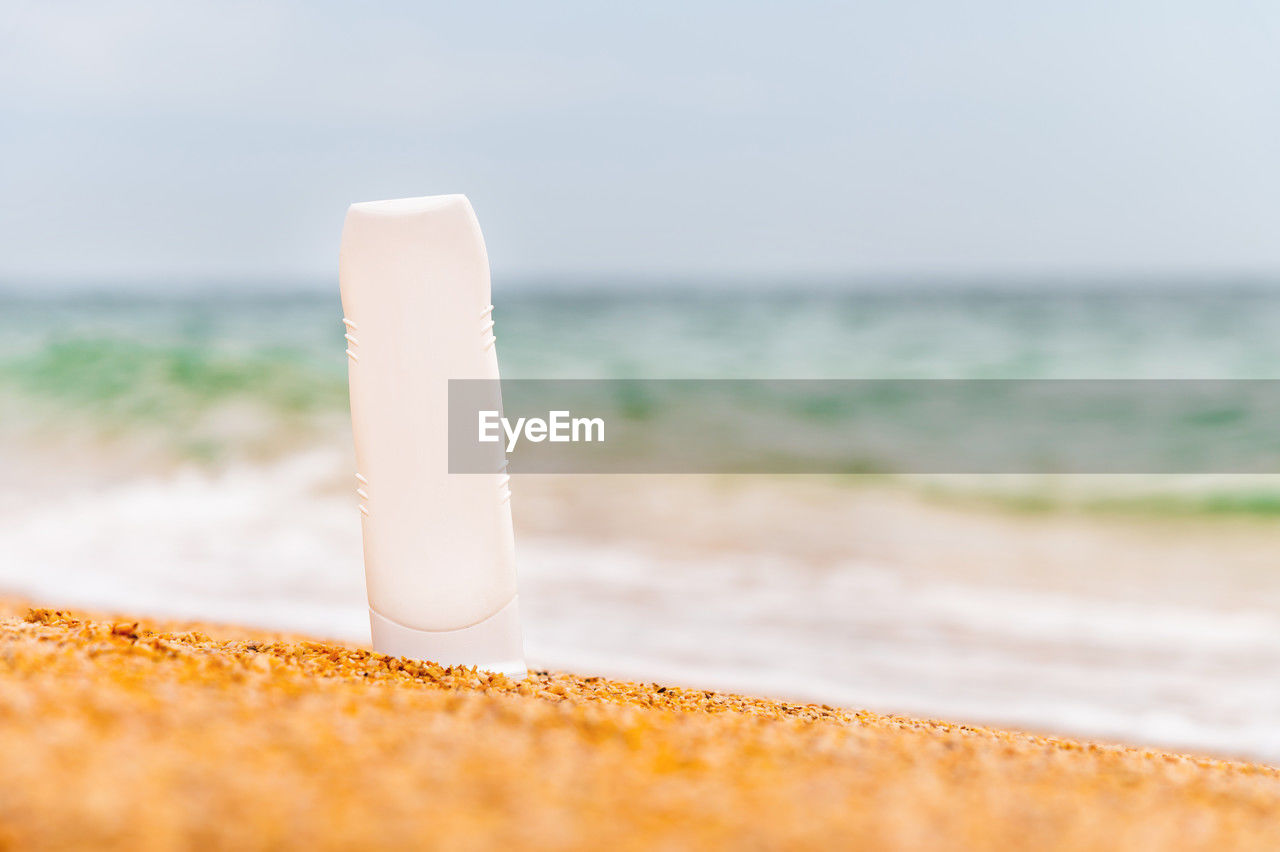 A bottle of sunscreen without a label on the beach on a sunny day. blank for advertising your cream