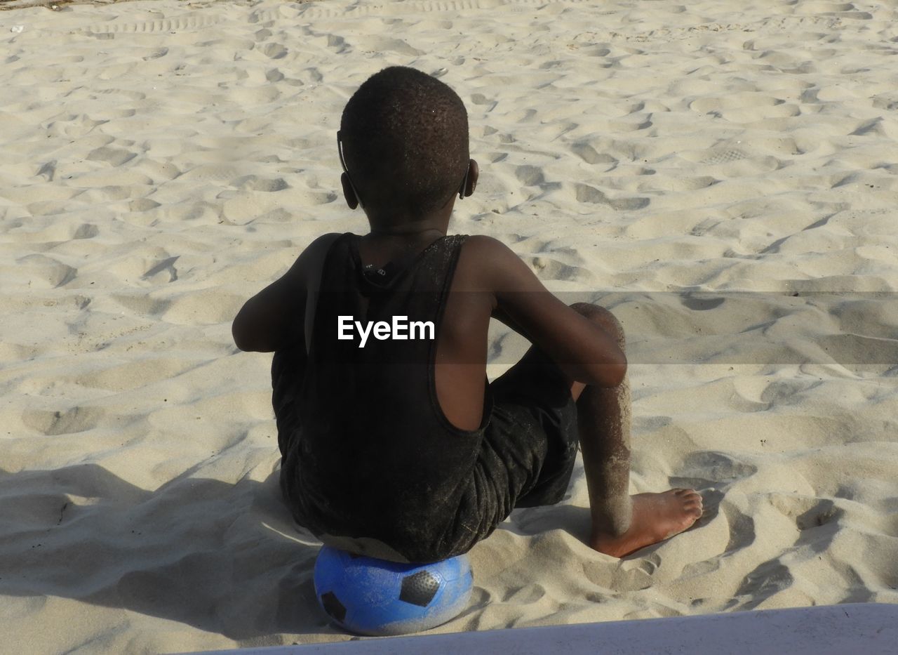 Rear view of boy sitting on ball at beach