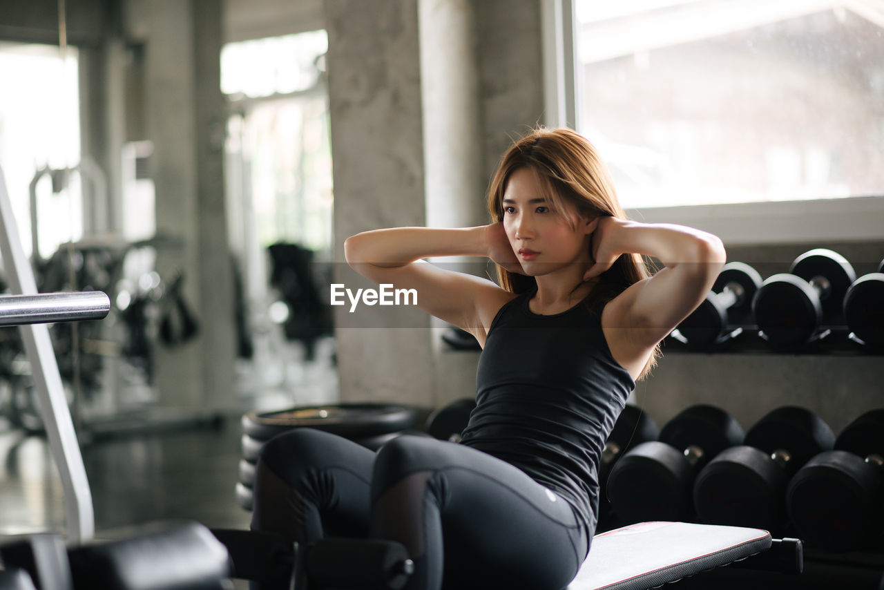 Young woman with hands behind head exercising in gym