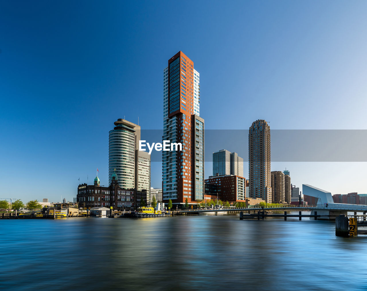 Modern buildings by river against blue sky