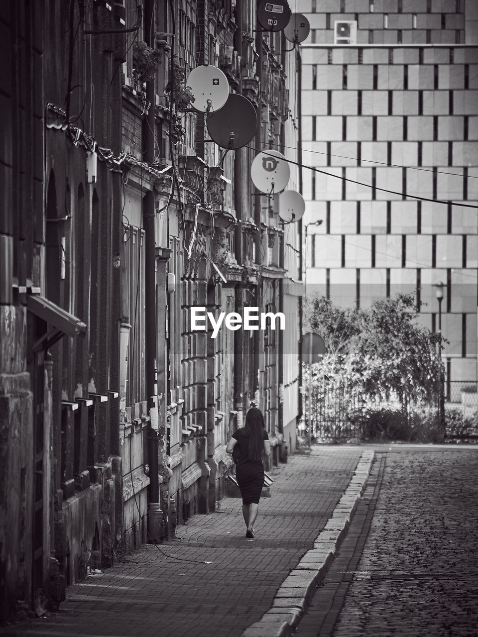 REAR VIEW OF MAN WALKING ON STREET AMIDST BUILDINGS IN CITY