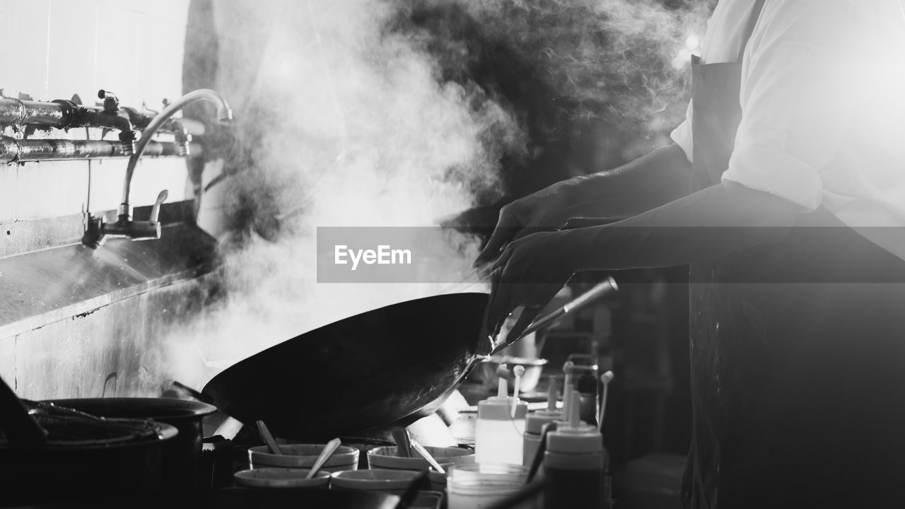 Chef stir fry busy cooking in kitchen. chef stir fry the food in a frying pan, smoke and splatter 