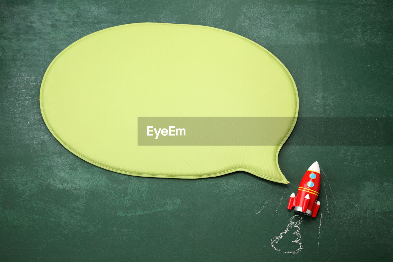 Directly above shot of blank speech bubble with toy rocket on blackboard