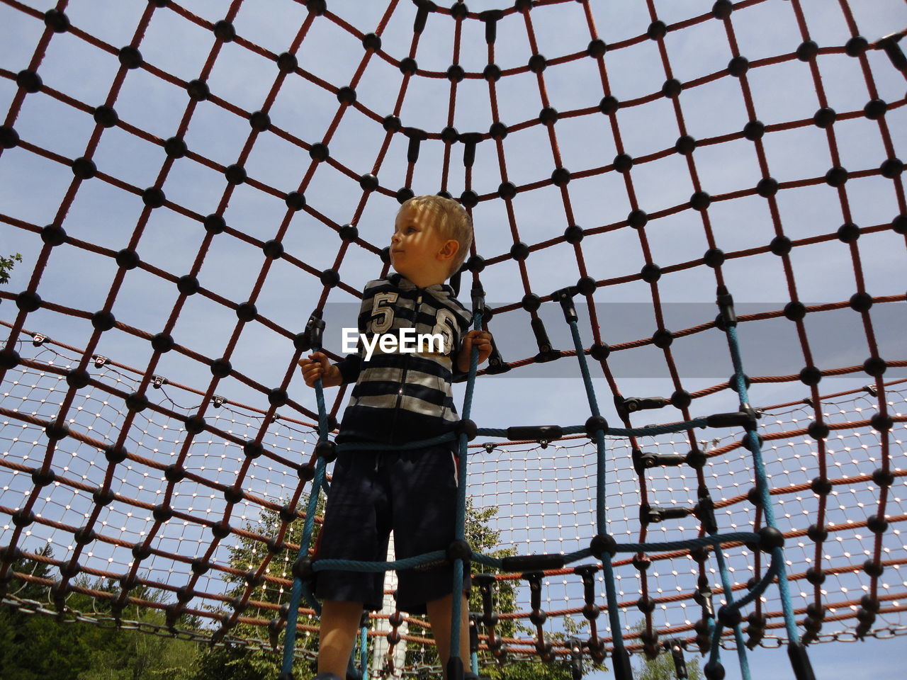 Boy climbing rope against sky at park