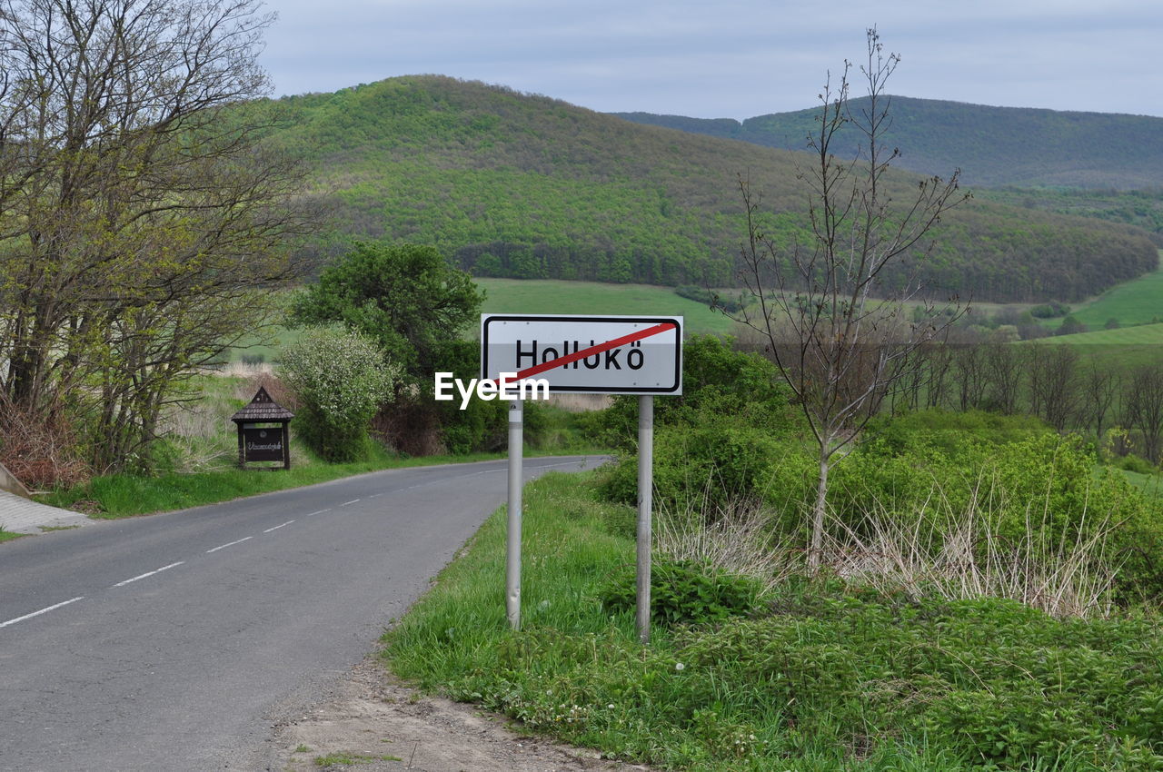 ROAD SIGN BY TREES ON MOUNTAIN AGAINST SKY