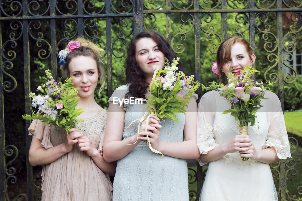 Portrait of friends with bouquet standing against gate