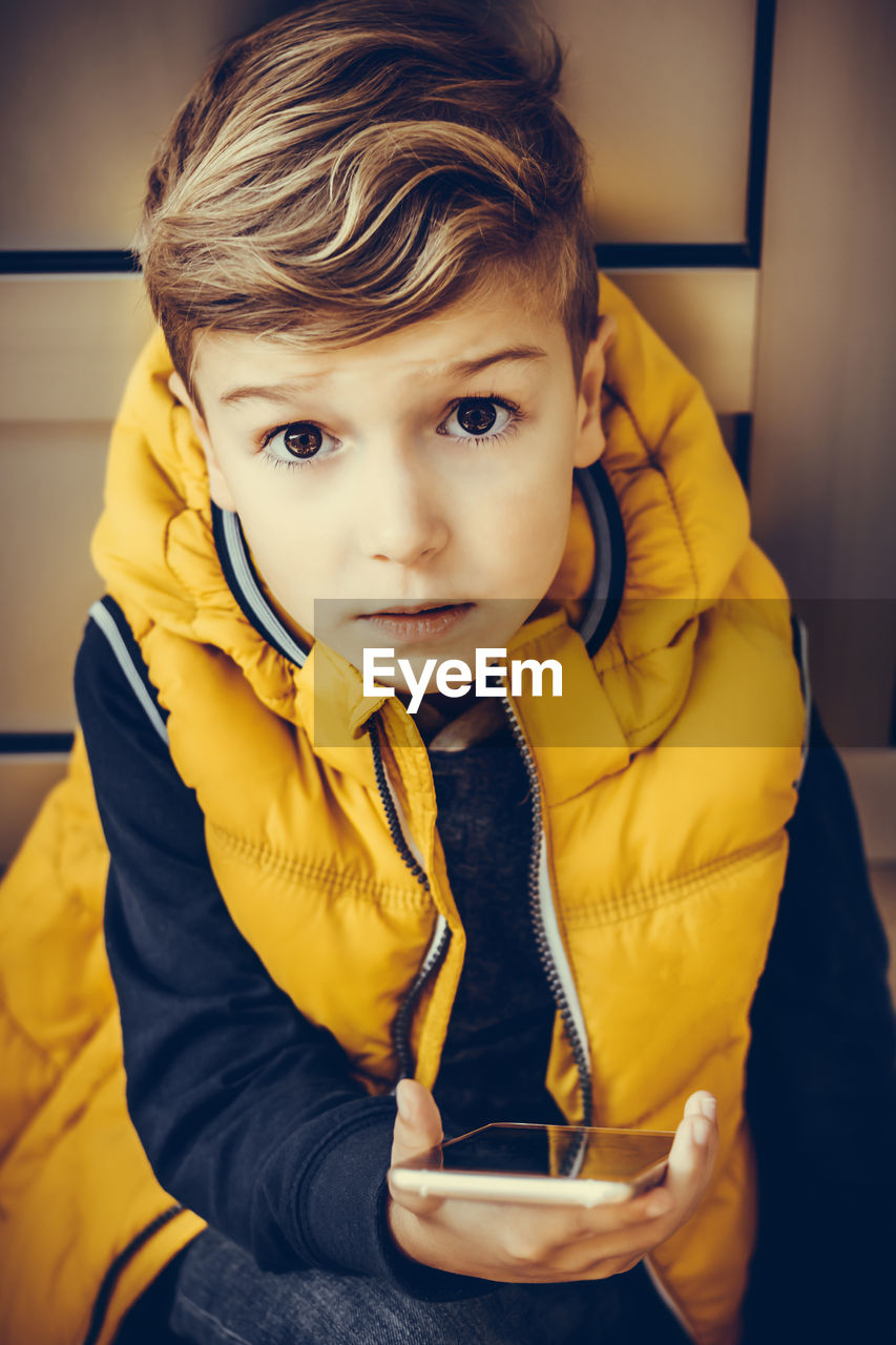 Small kid relaxing outdoors while using cell phone and looking at camera.