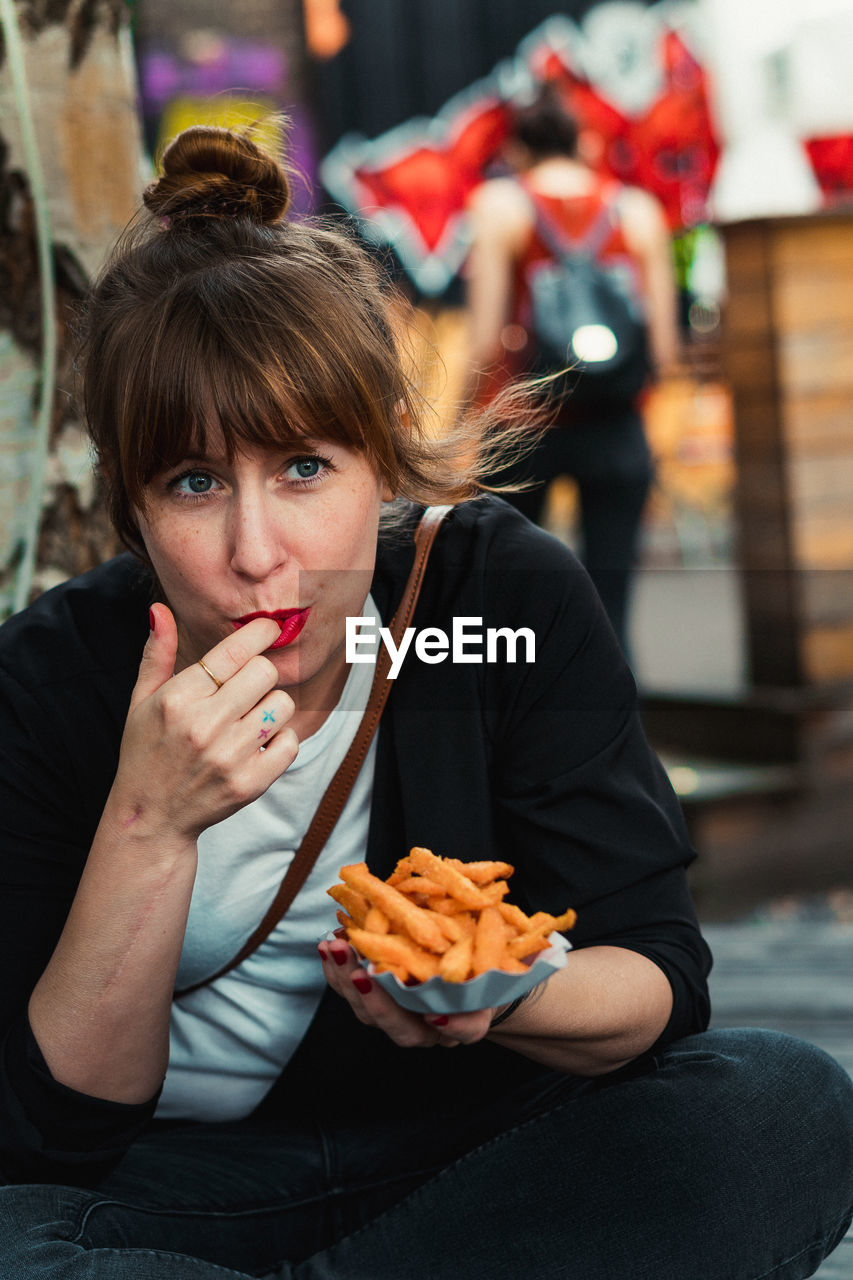 Portrait of young woman eating food in city