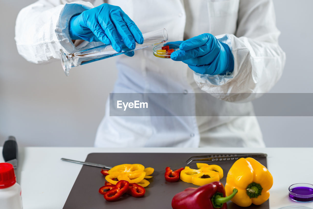 Midsection of scientist experimenting on bell peppers