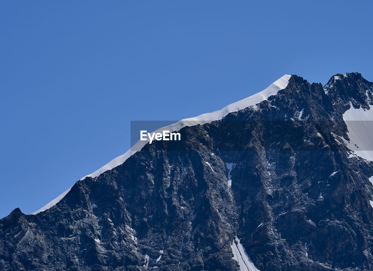 Low angle view of snowcapped mountains ridge against clear blue sky