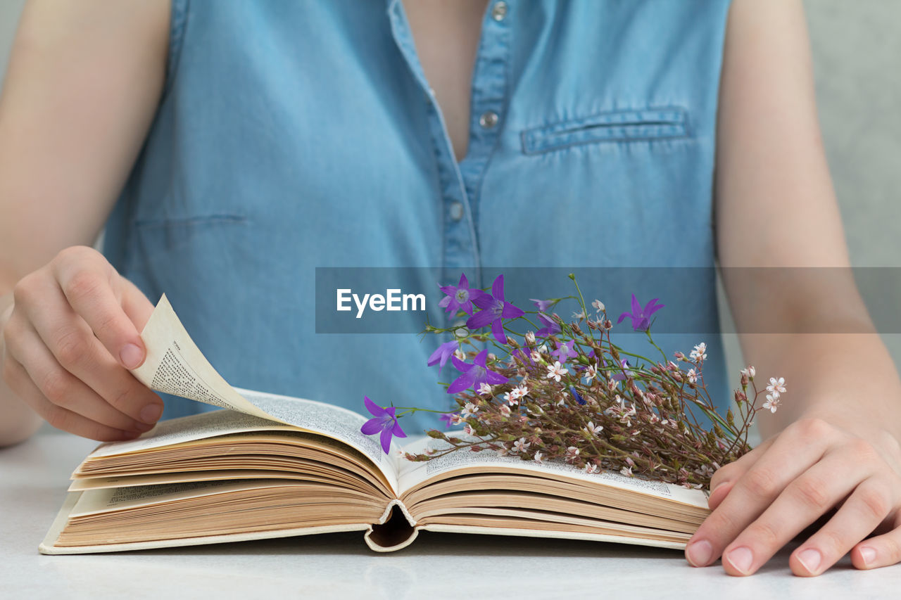 Midsection of woman reading book with flowers