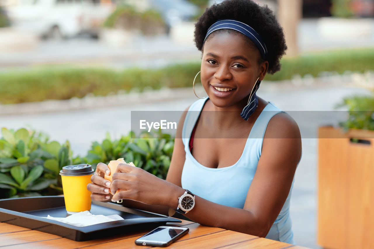 Cute african woman having lunch outdoors in city cafe. an african-american woman smiles