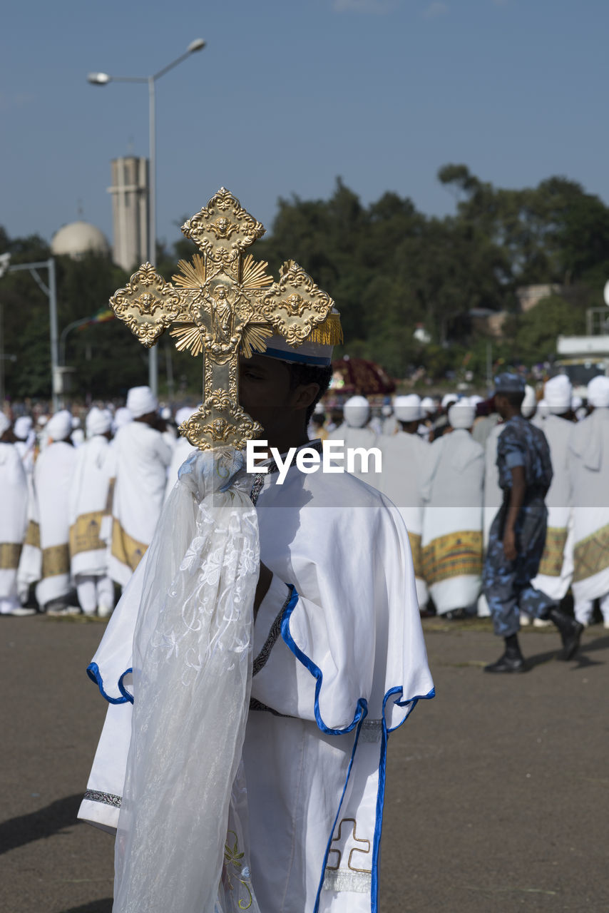 Man in traditional clothing holding cross on street